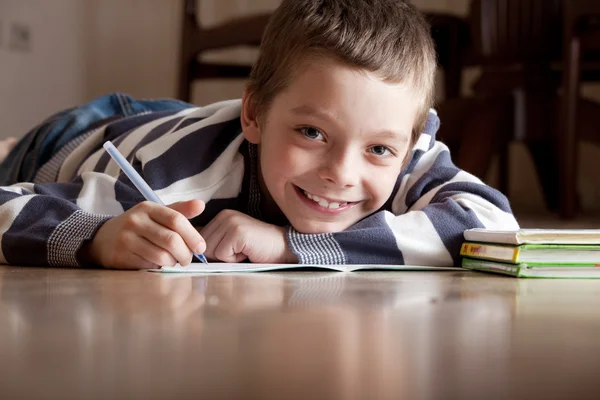 Pojke gör lektioner som ligger på golvet — Stockfoto