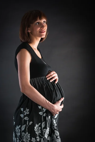 Удумлива вагітна жінка тримає живіт на сірому кінчику — стокове фото