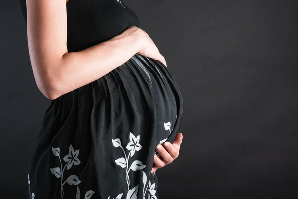 El estómago de la mujer embarazada en un vestido oscuro con colores blancos —  Fotos de Stock