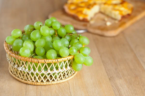 Cesta de vime cacho uvas verdes corte bolo de madeira — Fotografia de Stock