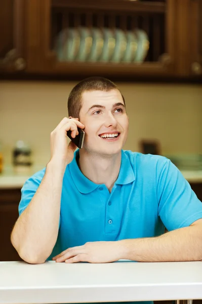 Молодой человек с мобильным телефоном на кухне — стоковое фото