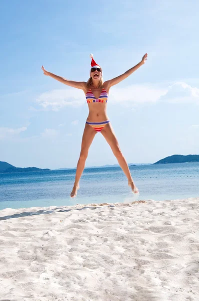 Молодая женщина прыгает на пляже в шляпе Санты — стоковое фото