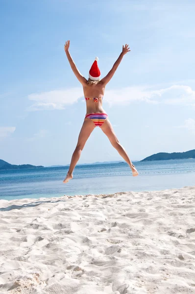 Mujer joven saltar en la playa en el sombrero de Santa Claus —  Fotos de Stock