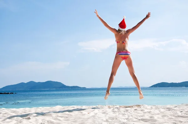 Молода жінка стрибає на пляжі в капелюсі Санти — стокове фото