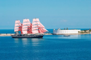 Sailing ship with red sails entering to the bay. clipart