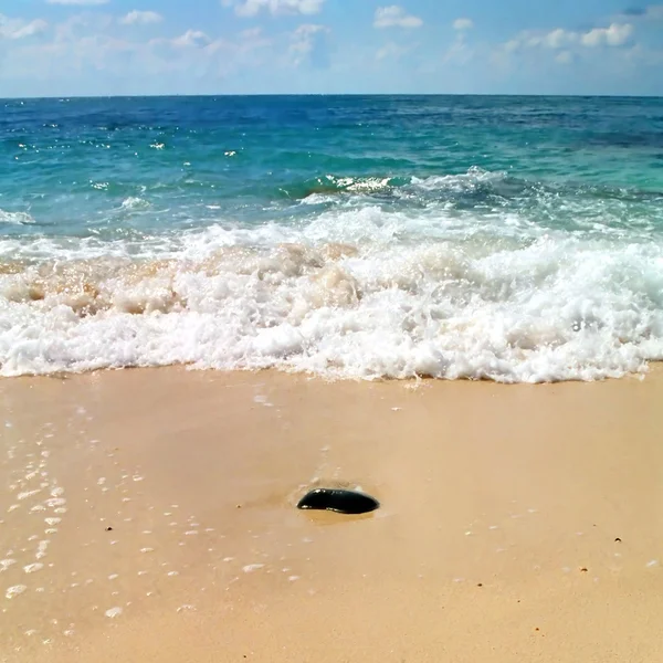 Камень в песке и волна позади него . — стоковое фото