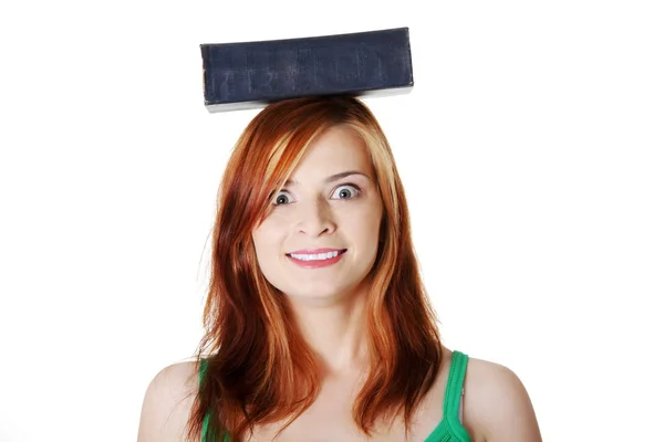 Sonriente adolescente chica sosteniendo libro en su cabeza . — Foto de Stock