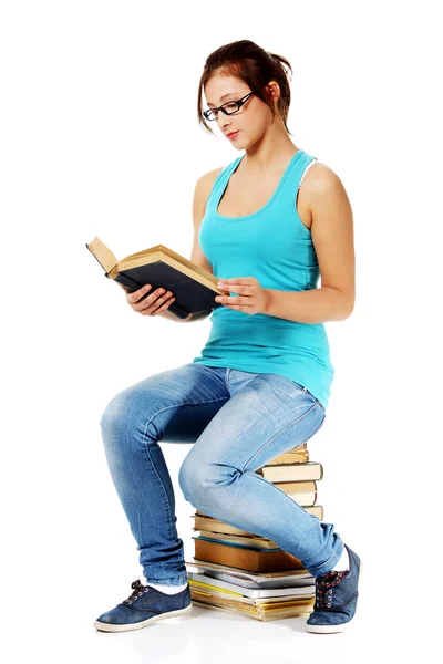 Teen student čtení knihy, sedící na knihách. — Stock fotografie