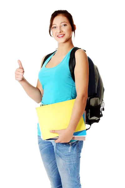 Улыбающаяся девушка-подросток с рюкзаком, держащая заметки и показывающая большой палец вверх — стоковое фото