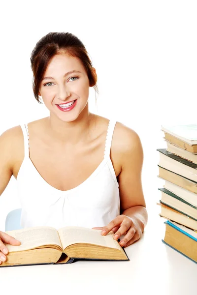 Улыбающаяся девушка сидит рядом с грудой книг . — стоковое фото