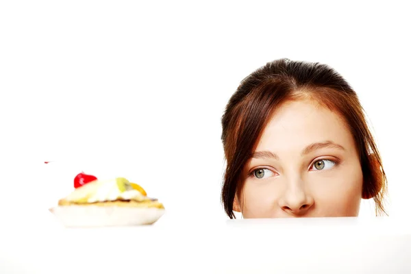 Menina escondida atrás da mesa e olhando para o bolo . — Fotografia de Stock