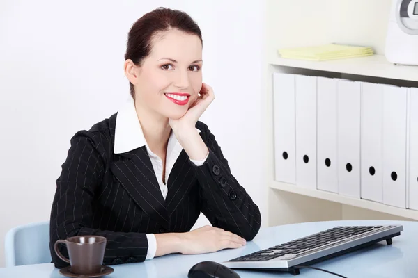 Uśmiechnięta kobieta siedzi w biurze. — Zdjęcie stockowe