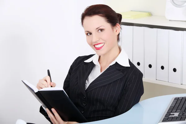 Деловая женщина, держащая в руках открытую тетрадь и ручку, сидит в офисе — стоковое фото