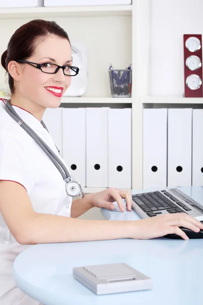 Attraktiva läkare sitter vid skrivbordet med datorn. — Stockfoto