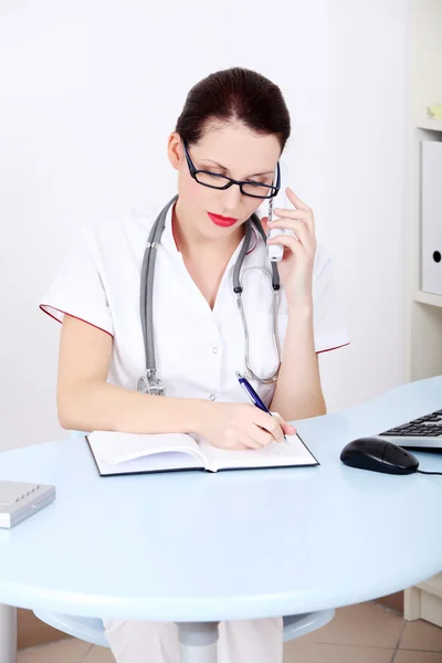 Kobieta lekarz rozmawia przez telefon i pisać. — Zdjęcie stockowe