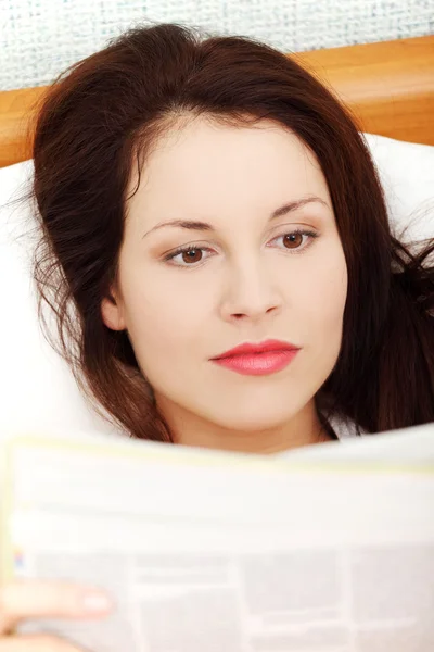 Piękna kobieta, czytanie gazety w łóżku. — Zdjęcie stockowe