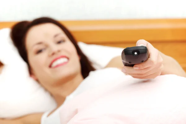 Bella donna a letto con un telecomando in mano . — Foto Stock