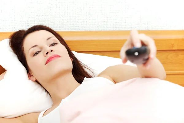 Krásná žena v posteli drží dálkové ovládání. — Stock fotografie