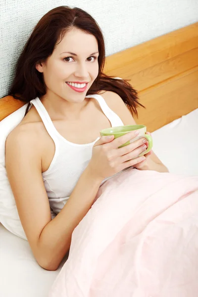 Mujer hermosa sosteniendo una taza de café en la cama por la mañana . —  Fotos de Stock