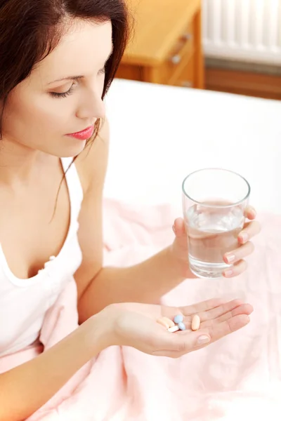 Mulher bonita segurando pílulas e um copo de água . — Fotografia de Stock