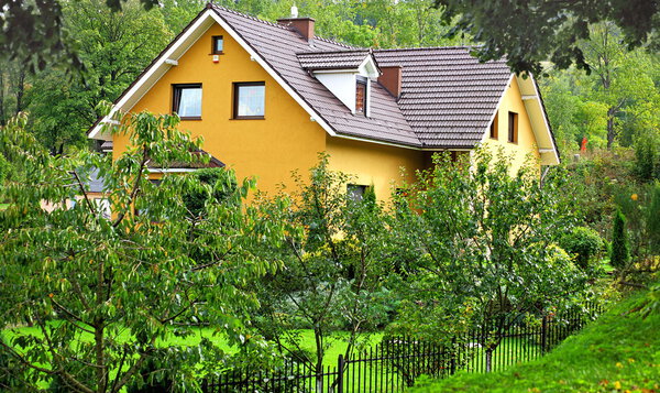 Yellow rural house hidden in green garden