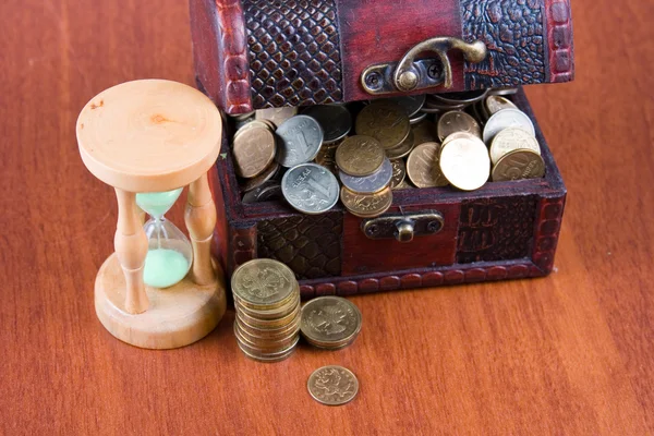 Открытый ящик с монетами и песочными часами — стоковое фото