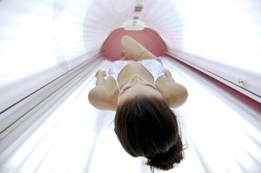 Beautiful young woman tanning in solarium clipart