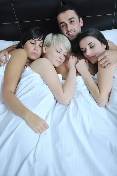 Jonge knappe man liggend in bed met drie meisjes — Stockfoto