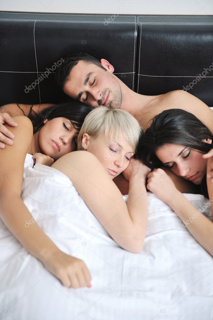 Young handsome man lying in bed with three girls