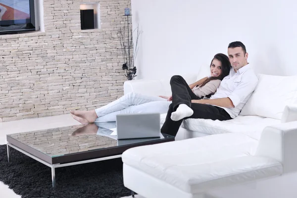 Радостная пара расслабиться и работать на ноутбуке компьютер в современном доме — стоковое фото