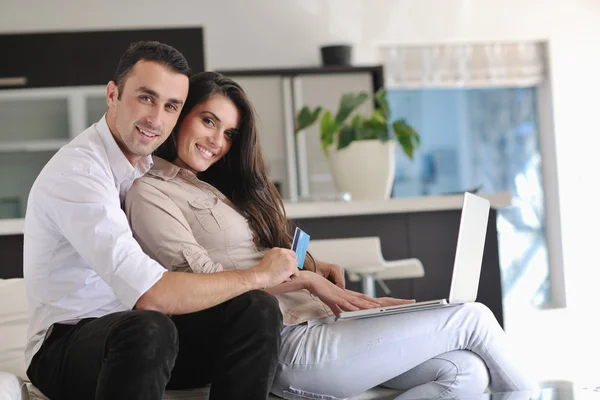 Радостная пара расслабиться и работать на ноутбуке компьютер в современном доме — стоковое фото