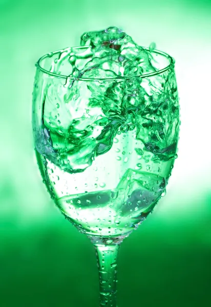 Glas met splash op groene achtergrond — Stockfoto