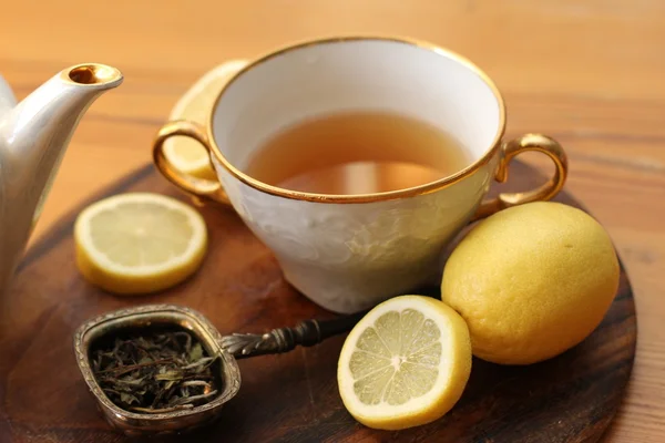 Taza de té, hojas de té y limones — Foto de Stock