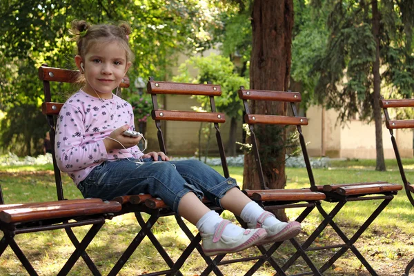 Liten flicka sitter i parken och lyssna på musik på telefonen — Stockfoto