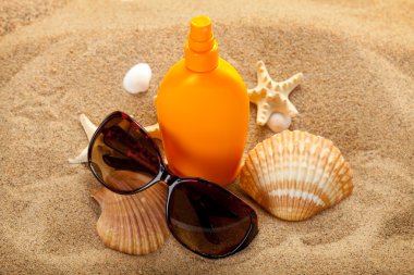 Summer beach - suntan oil and dark glasses on sand clipart