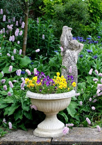 Stenen bloem container met viooltjes en een stenen beeld — Stockfoto