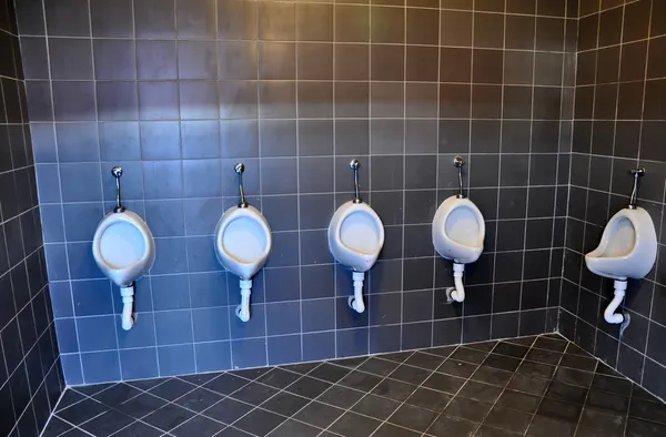 Bathroom urinals in a row with dark gray tiles — Stock Photo, Image