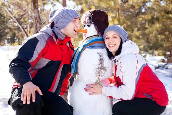 Couple with a snowman — Stock Photo, Image