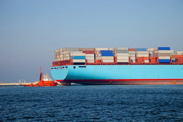 Nave container lascia il porto, assistita da un rimorchiatore . — Foto Stock