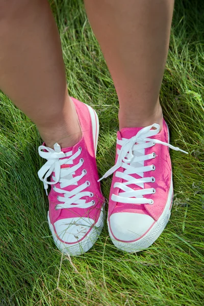Rosa Turnschuhe auf Mädchenbeinen im Gras — Stockfoto