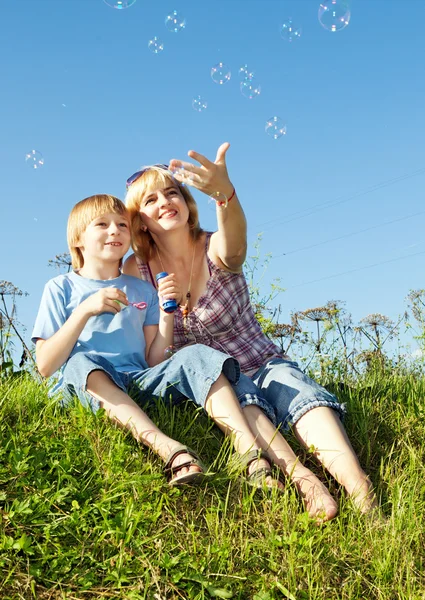 Boy and mother with soap bubbles against a sky — Stock Photo, Image