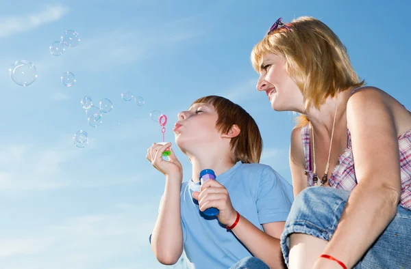 Boy and mother with soap bubbles against a sky — Stock Photo, Image