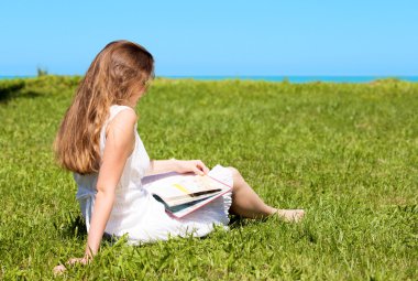 kız öğrenci oturup çim ve okuma ders kitabı