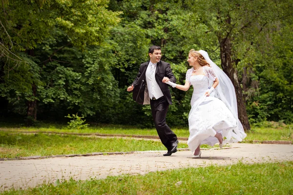 Happy bride and bridegroom running along the alley in the park — Stock Photo, Image