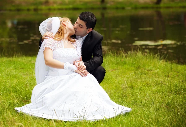 Recém-casados felizes na grama no parque — Fotografia de Stock