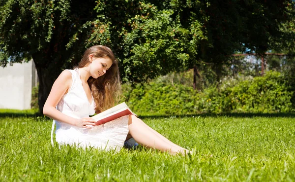女子学生の芝生と読み取りの教科書の上に座る — ストック写真