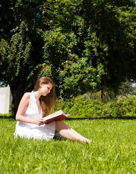 女子学生の芝生と読み取りの教科書の上に座る — ストック写真