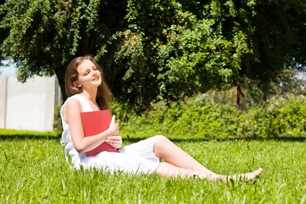 Menina-estudante sentar-se no gramado e lê livro didático — Fotografia de Stock
