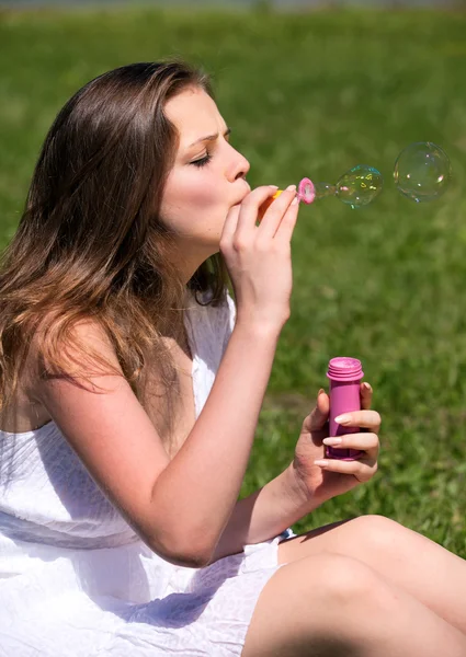 Chica joven soplando burbujas de jabón en el parque verde de verano —  Fotos de Stock