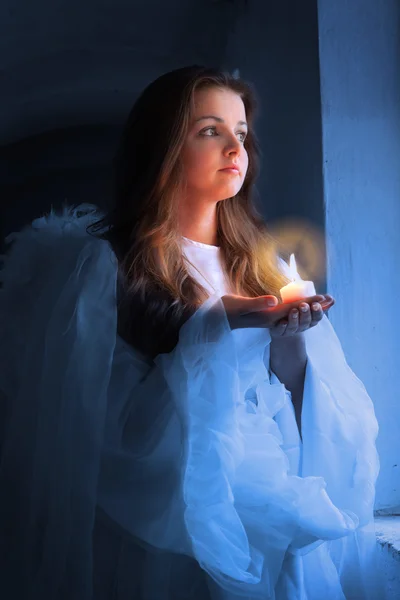 Retrato de um anjo com uma vela em pé perto da janela . — Fotografia de Stock